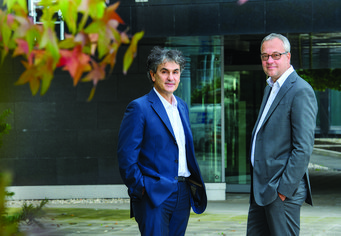 Die Direktoren des MPIfG im Hof des Institutsgebäudes Zwei Männer in Business-Anzügen stehen vor einem modernen Gebäude mit Glasfront.