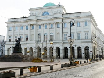 Institut für Philosophie und Soziologie, Polnische Akademie der Wissenschaften (IFiS PAN) Ein großes neoklassizistisches Gebäude mit einer grünen Kuppel, dekorativen Straßenlaternen und einer Statue einer sitzenden Figur auf einem Sockel davor.