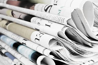 Ein Stapel gefalteter Zeitungen zeigt verschiedene Überschriften und Bilder in einer Mischung aus Farbe und Schwarzweiß, die Details von Schlagzeilen und Artikeln erkennen lassen.