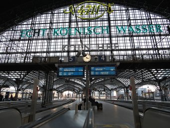 Hauptbahnhof Köln Ansicht des Kölner Hauptbahnhofs mit leeren Gleisen, einer zentralen Uhr und einem prominenten Echt Kölnisch Wasser-Werbeschild.