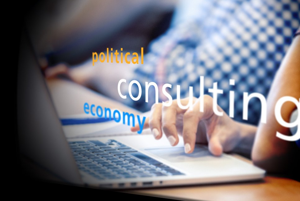 Close-up of hands typing on a laptop keyboard. Overlay words "political," "consulting," and "economy" suggest a focus on these topics.
