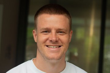 Smiling person in a white shirt against a blurred background. The tone is warm and approachable, conveying friendliness and positivity.