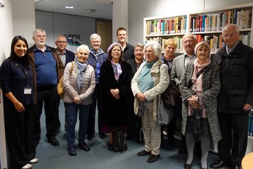 The photo shows a group of senior citizens in front of a bookshelf.