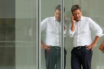 Robert Habeck telefoniert mit ernster Miene vor einer verspiegelten Fläche