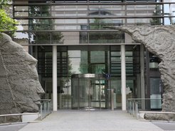Modern glass facade of the Max Planck Society building, flanked by stone sculptures.