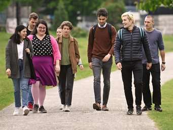 A diverse group of seven individuals casually strolling along a park path, surrounded by green grass.