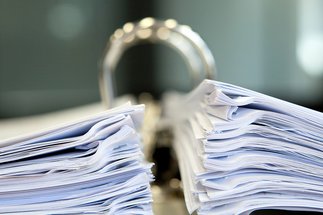 Nahaufnahme eines großen offenen Ordners, gefüllt mit zwei dicken Papierstapeln, der auf einem Schreibtisch in einer professionellen Büroumgebung steht.