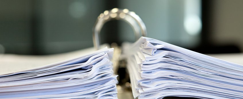 A close-up view of a large open binder filled with two thick stacks of paper, placed on a desk in a professional office environment.