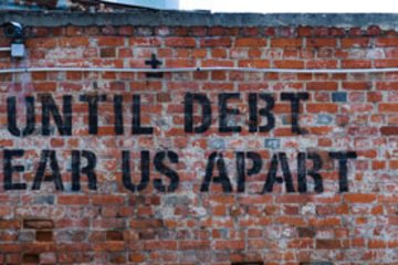 On a red brick wall, in large black letters, it reads "Until debt tear us apart". A surveillance camera is mounted at the top left, with cables running beside it.