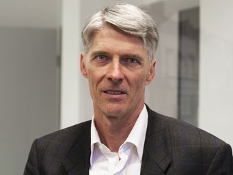 Mark Ebers has been a member of the IMPRS-SPCE Faculty from 2007 to 2021 The photo shows an individual of the species Homo sapiens. He has gray hair, is wearing a dark suit and a white shirt with a collar that is open at the neck. The hair is already gray, but still full and shiny. The hair is parted on the right side and neatly combed. The mouth is half open, and the face shows the hint of a tentative smile that can be discerned with sufficient goodwill. The evidence suggests that the scene is set in an office.