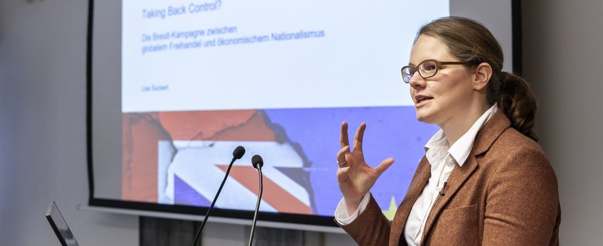 Die Präsentation enthält eine Folie mit dem Titel „Die Kontrolle zurückgewinnen?“, die sich mit dem Gleichgewicht zwischen wirtschaftlichem Nationalismus und Freihandel im Zusammenhang mit dem Brexit befasst und ein Bild der britischen Flagge zeigt.